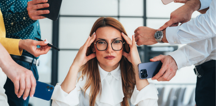 Woman sitting at a desk with her hands pressed to her temples, suggesting stress or overwhelm.